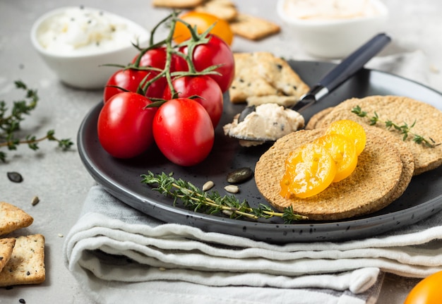 Dunne krokante volkoren crackers met roomkaas en tomaten op een zwarte plaat.