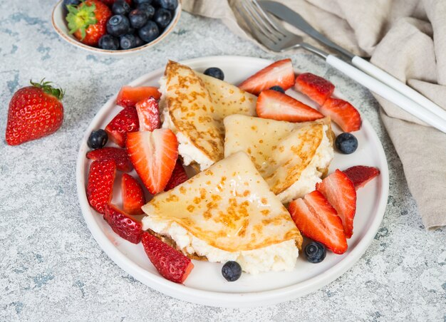 Dunne pannenkoeken met ricotta kaas en verse aardbeien op een grijze betonnen achtergrond.