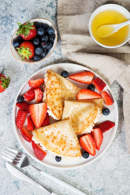 Dunne pannenkoeken met ricotta kaas en verse aardbeien op een grijze betonnen achtergrond.