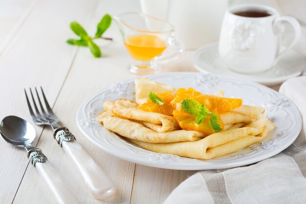 Dunne pannenkoeken met sinaasappel-citrussaus voor ontbijt op een lichte ondergrond