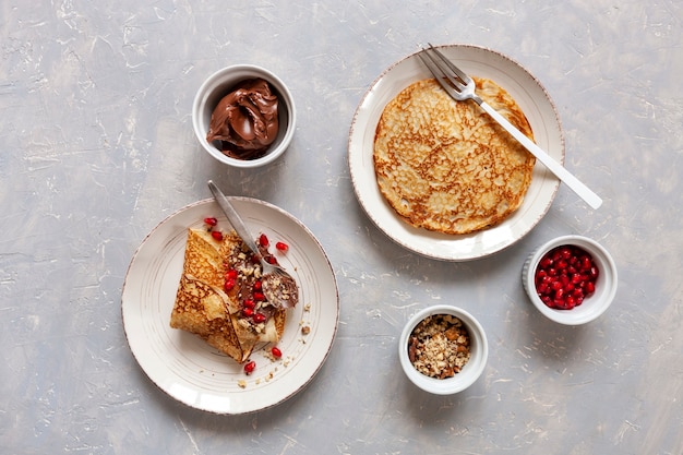 Dunne pannenkoeken op plaat met granaatappel, chocolade en walnoten op lichte achtergrond. Bovenaanzicht, close-up