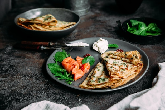 Dunne pannenkoekjes met kruiden, zalm en roomkaas op een bord