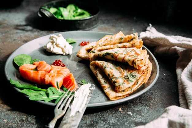 Dunne pannenkoekjes met kruiden, zalm en roomkaas op een bord