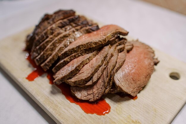 Foto dunne plakjes roastbeef met bloed liggen op een houten snijplank op de tafel.