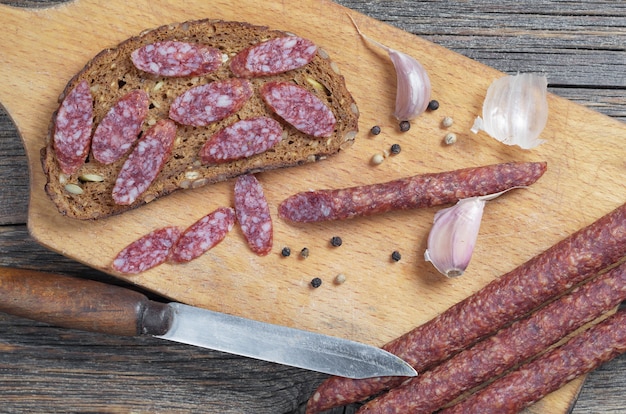 Dunne rookworst, brood, knoflook en peper op snijplank bevindt zich op oude houten tafel