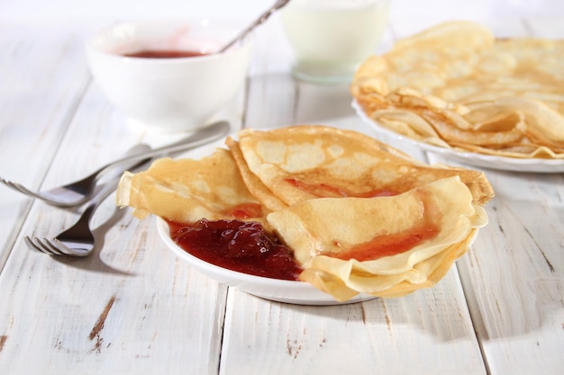 Dunne warme pannenkoeken met aardbeienjam op een witte houten tafel Holiday Maslenitsa