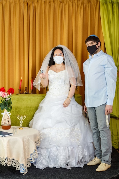 Durante la cerimonia della chuppah a un matrimonio ebraico nella sinagoga, gli sposi stanno accanto allo sposo tenendo un bicchiere di vino in mano agli sposini con una maschera protettiva