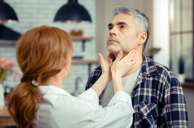 Durante la visita medica. un bell'uomo maturo che tiene la testa alta mentre si trova di fronte al dottore