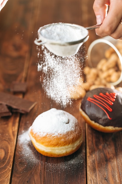 Photo dusting the donut with powdered sugar on the wooden table