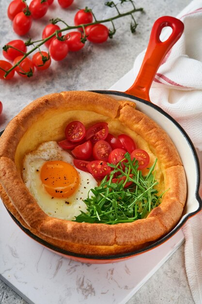 Dutch baby pancake Fresh homemade Dutch Baby pancake with fried egg tomato and green arugula in reed castiron pan on light gray concrete rustic table Flat lay close up