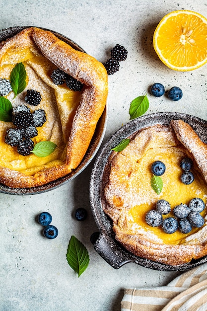 Dutch baby pancake with berries and lemon in cast iron frying pan, top view.