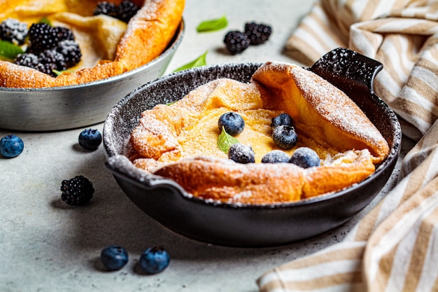 Dutch baby pancake with berries and lemon in cast iron frying pan.