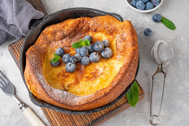 Блинчик Dutch Baby со свежей черникой и мятой, посыпанный сахарной пудрой, в железной сковороде