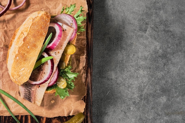 Dutch sandwich with herring, pickled cucumbers and red onions on a paper lining. Ingredients on a cutting board. Layout on the table, copy space