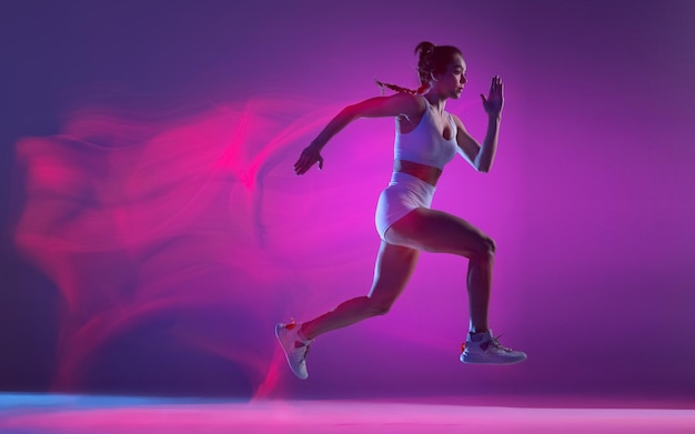 Фото Динамический портрет молодой спортивной женщины, тренирующейся на фиолетовом фоне в неоновом свете со смешанными огнями