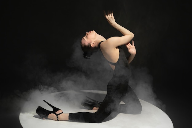 Динамический портрет молодой гибкой танцовщицы, танцующей на темном студийном фоне в центре внимания