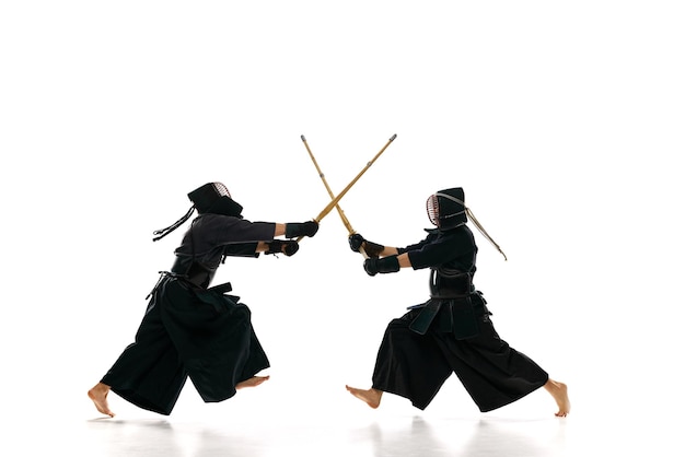 Dynamisch beeld van twee mannen professionele kendo-atleten die trainen met bamboe shinai-zwaard tegen witte studioachtergrond