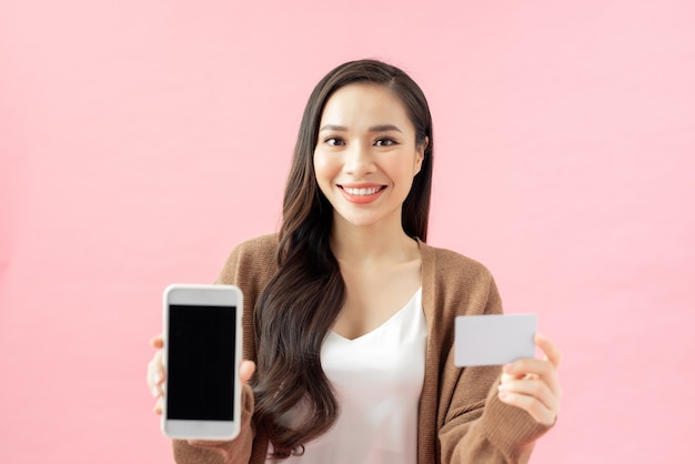 Eコマース、ショッピング、ライフスタイルのコンセプト。アジアの女の子は、オンラインショッピング、注文追跡、携帯電話の保持、画面の表示、クレジットカードの素晴らしいアプリケーションを見つけました
