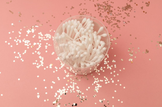 Ear cotton swabs in a clear cup on a pink background