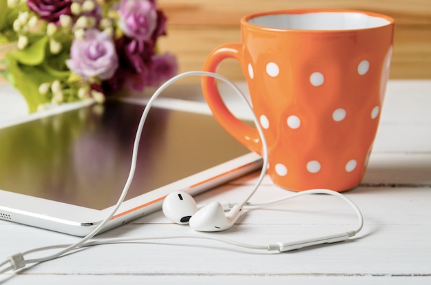 ear pods headphone tablet with orange cup of cofee on white wooden table