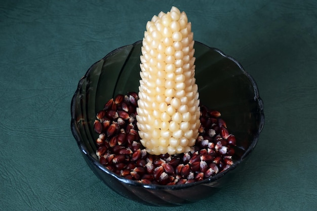 An ear of popcorn corn lies in a plate with darkcolored popcorn grains