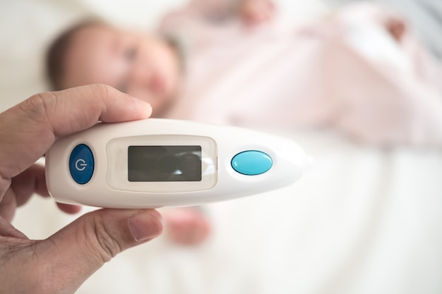 Ear Thermometer in parent hand with blurred new born baby 