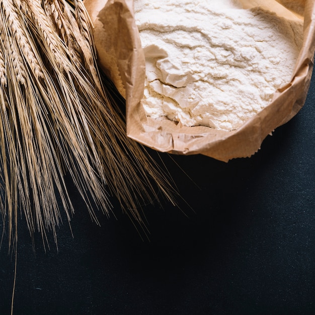 Photo ear of wheat and flour in paper bag on black background