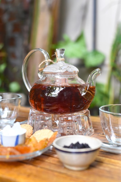 Earl Grey tea in glass teapot with cups and crystalized fruits on wooden table