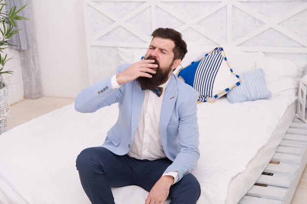 Early awakening. Man formal suit sit on bed. Businessman before difficult working day. Thoughtful groom before wedding. Morning time. Morning habits. Bearded hipster in bedroom. Morning thoughts.