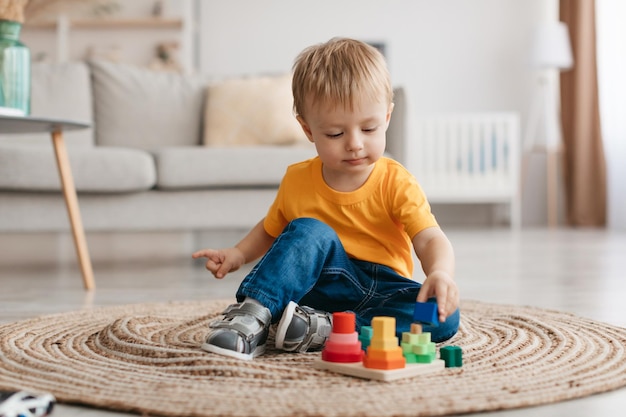 初期の開発コンセプト小さな幼児の男の子が家に座って教育用木のおもちゃで遊んでいます