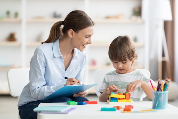 Sviluppo dei primi bambini ragazzino carino che gioca a una donna specialista del gioco di geometria logica con blocco note