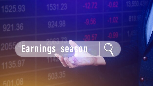 Earnings season hand holding with written in search bar with the financial data visible on background Reports Stock Market Ticker