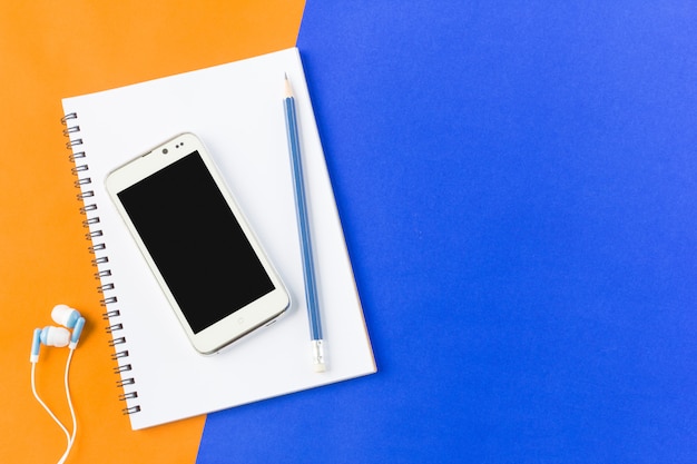 Earphone smartphone and notebook in top view on blue and orange background