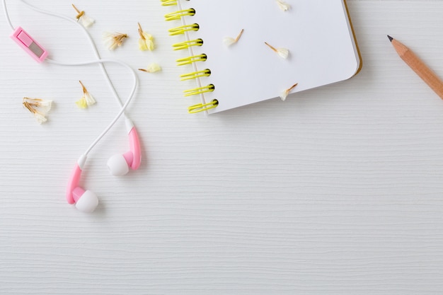 Earphones and notebook with flower on white table