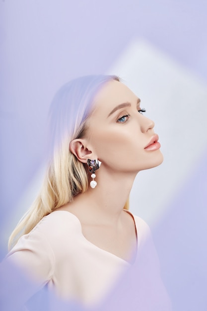 Earrings and jewelry in ear of a sexy blonde woman through a transparent colored fabric