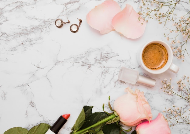 Earrings; lipstick; roses; nail varnish bottle; coffee cup and baby's-breath flower on textured background