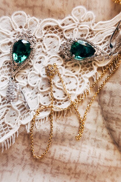 Earrings with emerald and a gold chain with a pendant on white lace