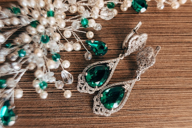 Orecchini con un grande smeraldo e un ornamento di perline bianche su sfondo marrone con un rough