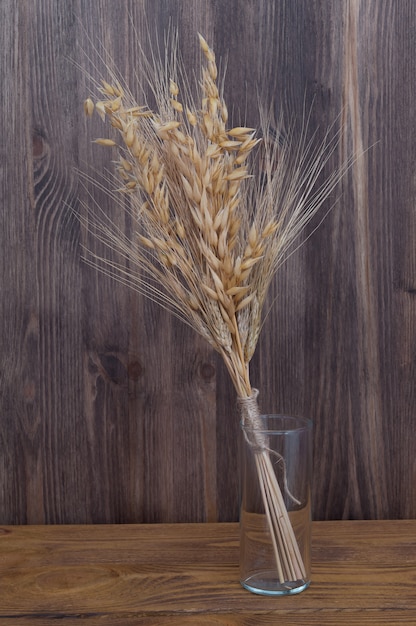 Ears of wheat and barley in a glass vase on the background of wooden boards.