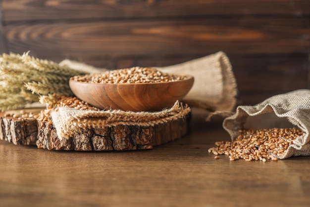 Колосья пшеницы и миска зерен пшеницы на коричневом деревянном фоне