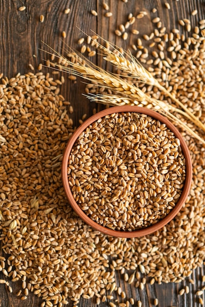 Ears of wheat and bowl of wheat grains on wooden background