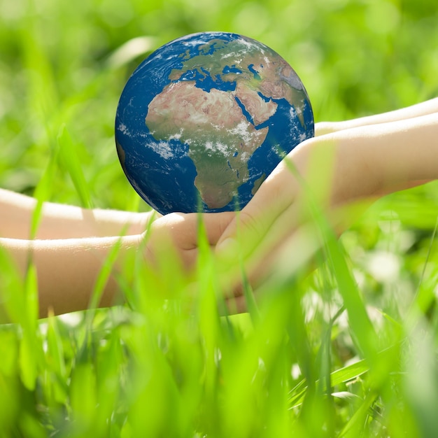 緑の草のぼやけた背景に対して子供の手の地球NASAによって提供されたこの画像の要素