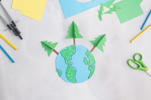 Earth cut from paper around trees earth day concept kids paper craft high quality photo