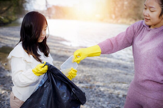 Earth Day-concept Vrouw en dochter halen afval op in vuilniszakken opruimen in de natuur tot recycling in hun gemeenschappen maken rivier schoon en beschermen het milieu tegen vervuilingsbehoud Natuur