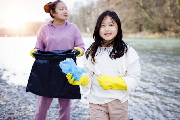 Earth day-concept vrouw en dochter halen afval op in vuilniszakken opruimen in de natuur tot recycling in hun gemeenschappen maken rivier schoon en beschermen het milieu tegen vervuilingsbehoud natuur