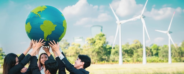 Концепция Дня Земли с большим земным шаром, которую держит команда азиатских бизнесменов, пропагандирующая экологическую осведомленность с использованием экологически чистой и возобновляемой энергии с ветряной турбиной для более зеленого будущего Круговорот