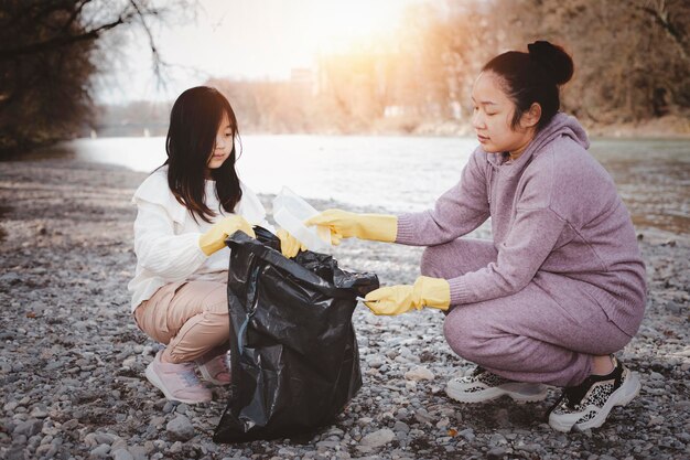 写真 アースデイのコンセプト女性と娘は、自然の中でゴミ袋にゴミを拾い、地域社会でリサイクルし、川をきれいにし、環境を汚染防止から守ります。