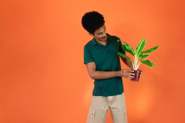 アースデイハンサムな若い黒人男性、オレンジ色の背景に分離された植物を保持している緑のシャツ