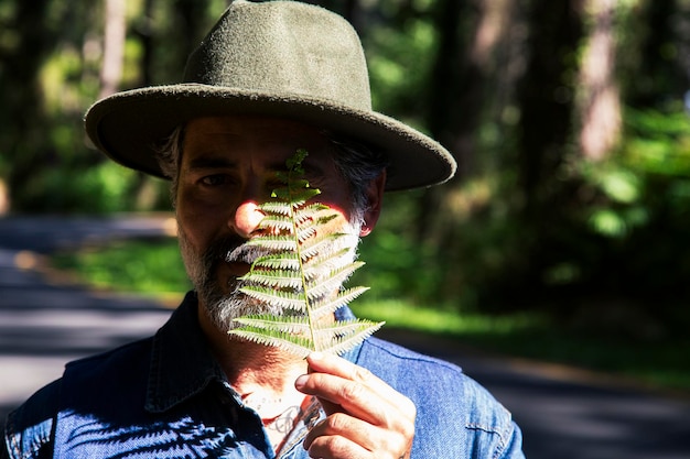 Giornata della terra e amore per il concetto di natura con un uomo attraente con una foglia di felce che copre un occhio e godersi le attività ricreative della natura all'aperto