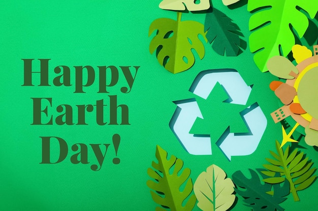 Earth Day recycling sign and paper leaves on green background with text top view